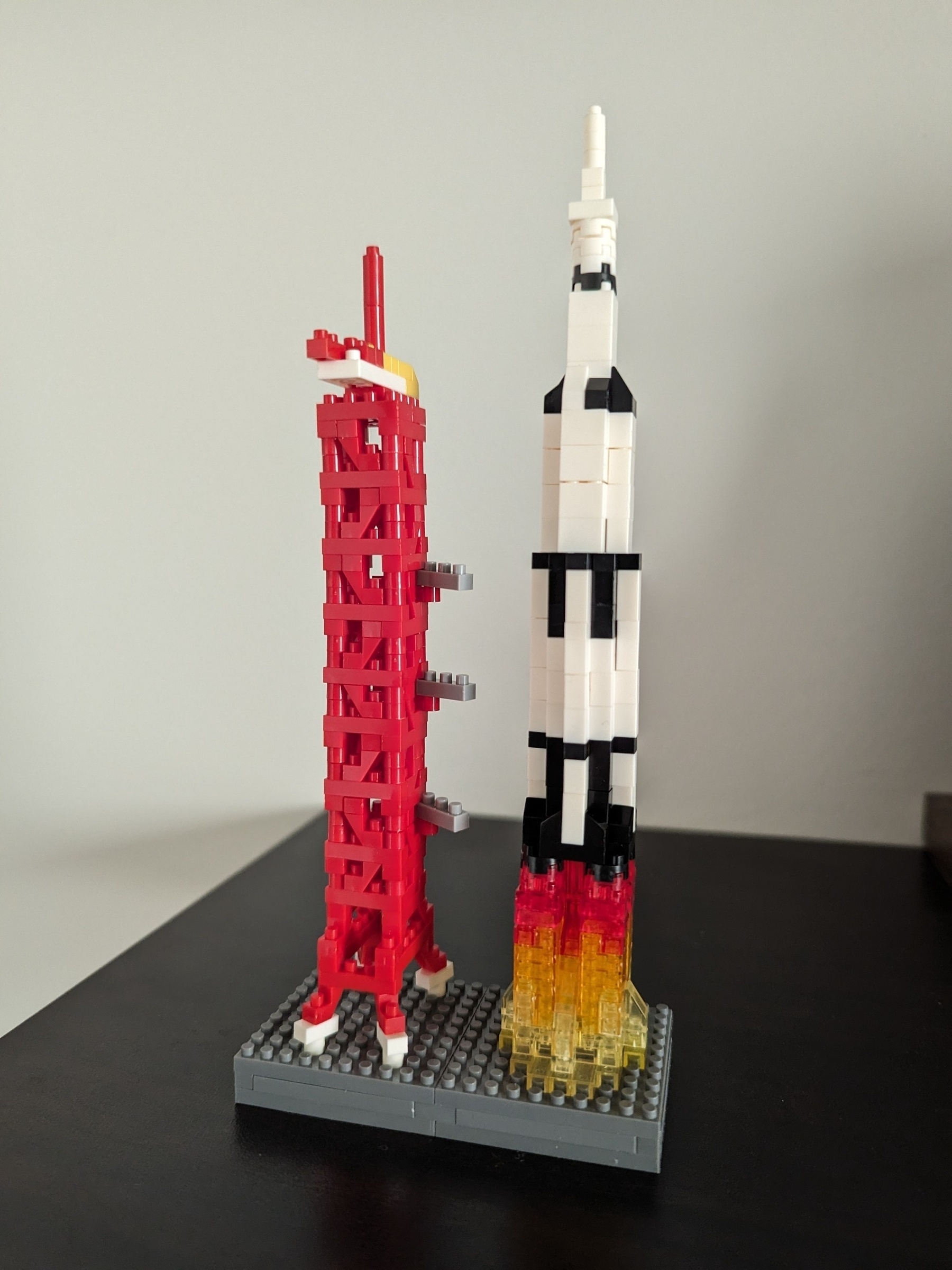 Six inch tall Lego model of a Saturn five rocket blasting off of a launch pad.
