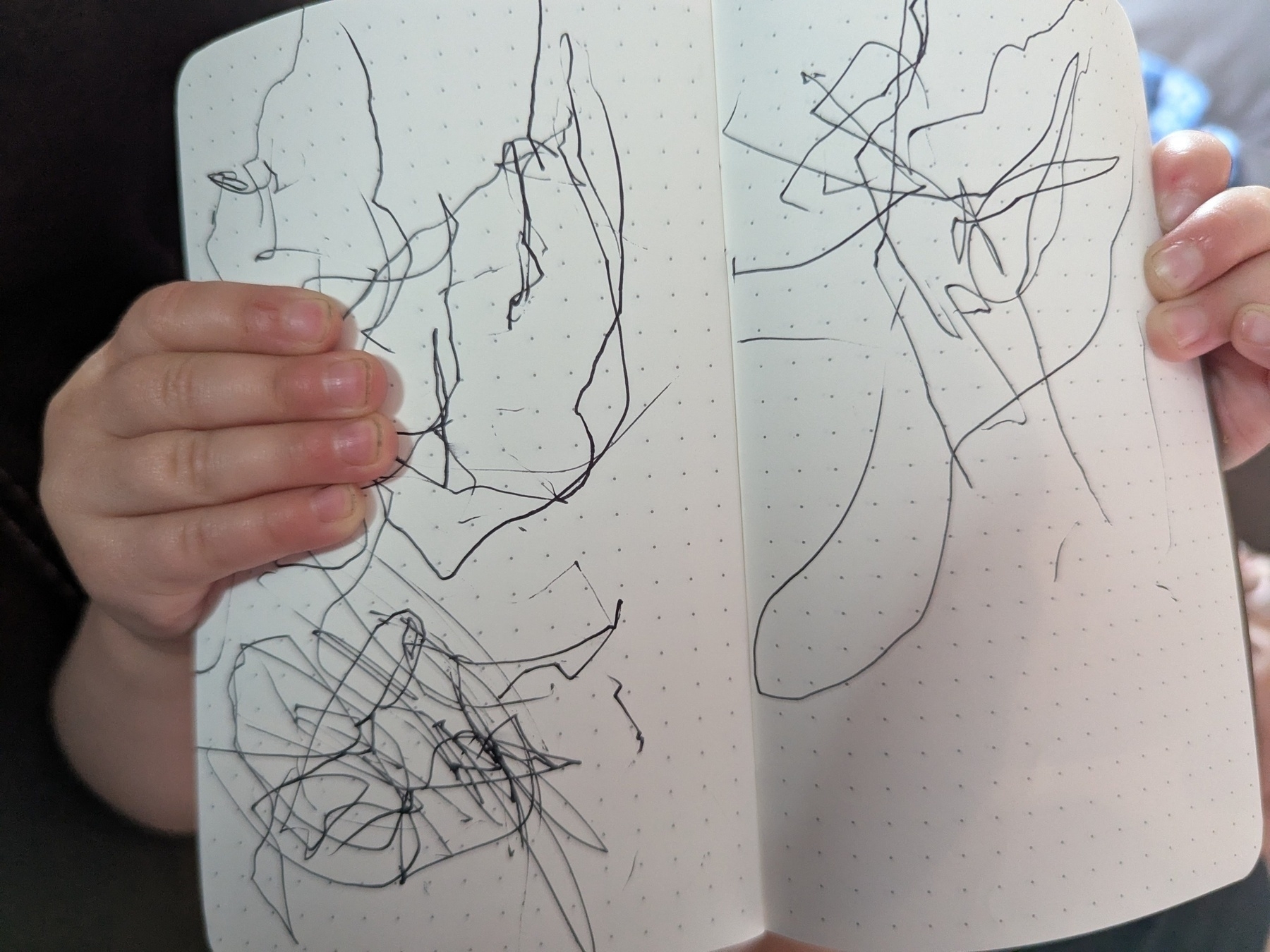 A child is holding open a notebook filled with scribbles.